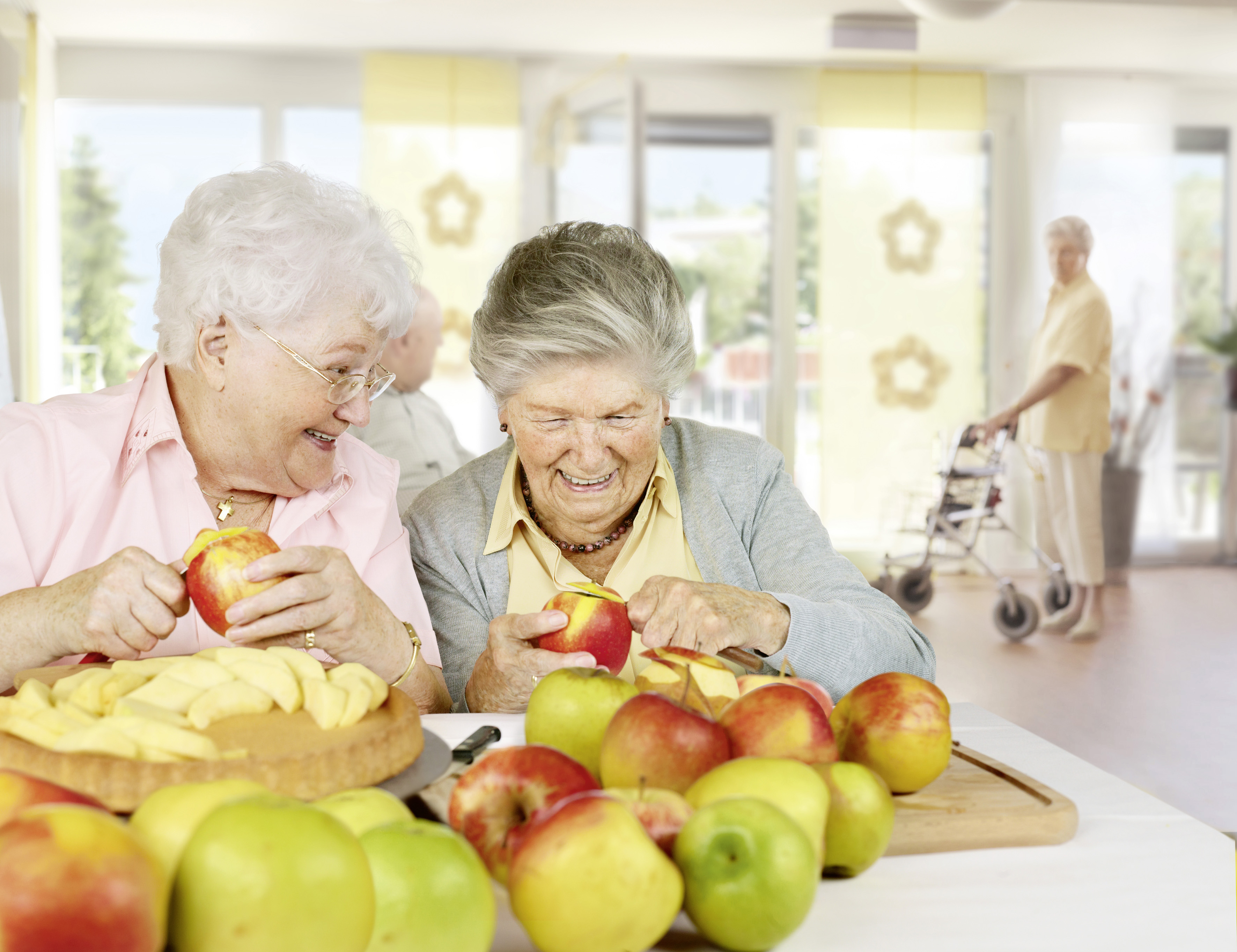 Zwei Seniorinen schälen gemeinsam Äpfel und lachen.